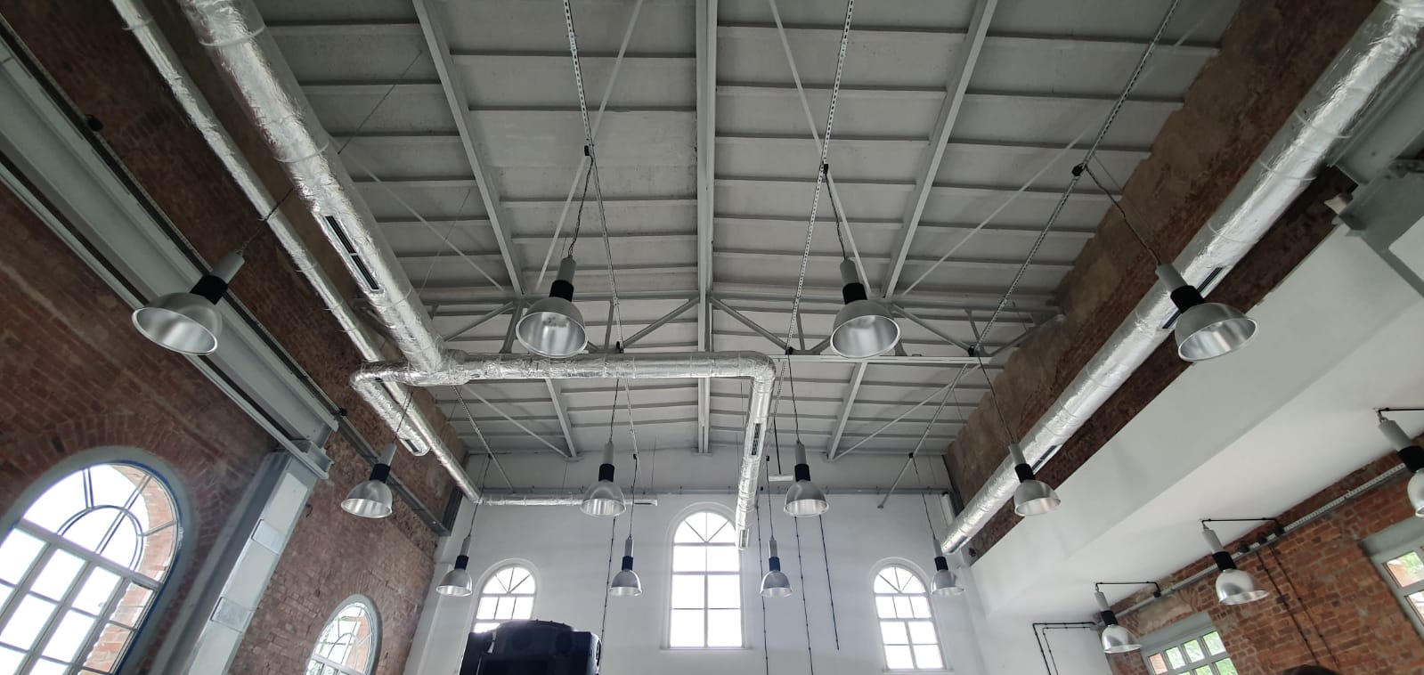 Ignacy 05 2020 1 Industrialne wnętrze, ściany z czerwonej cegły, stalowe konstrukcje. Z sufitu zwisają lampy.