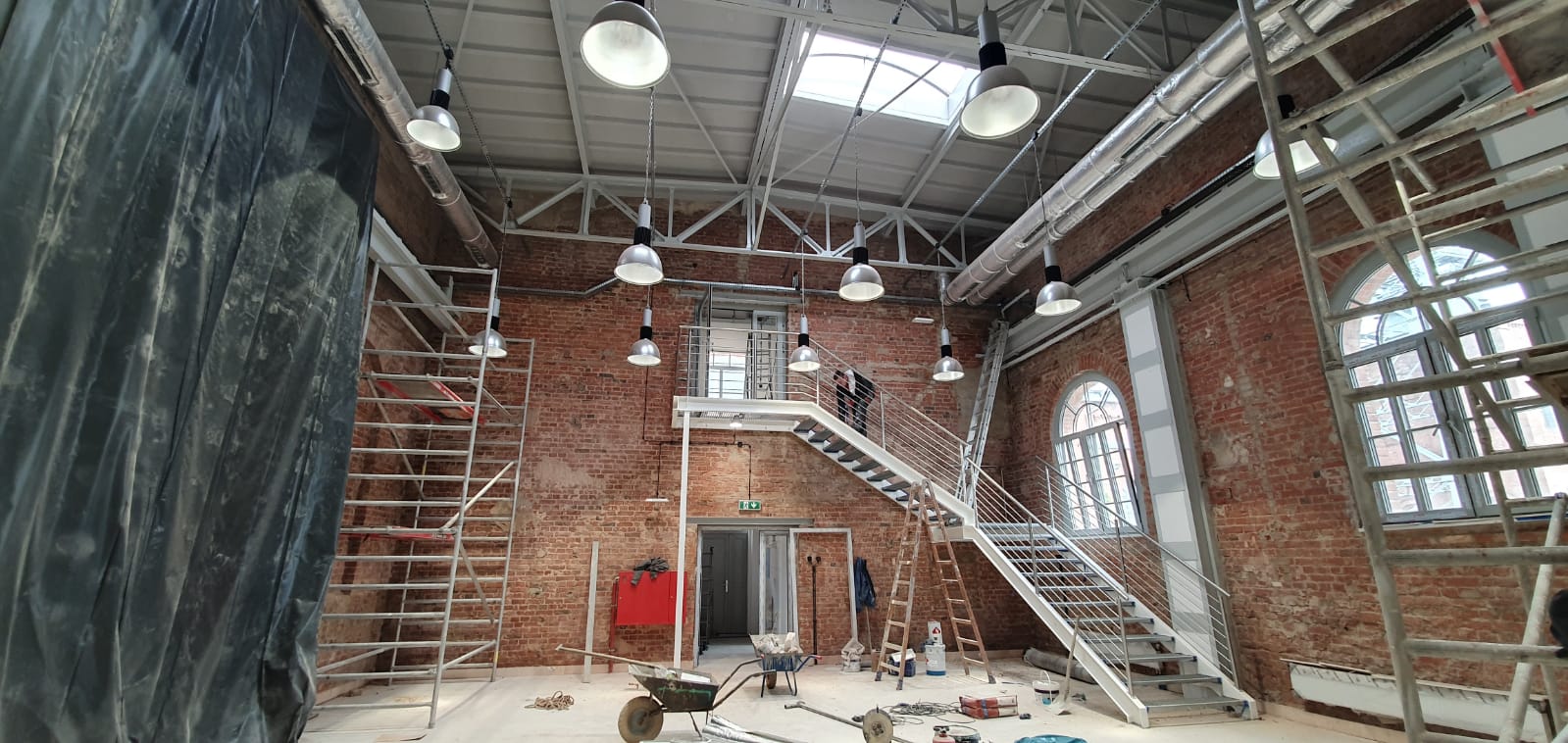 Ignacy 05 2020 4 Industrialne wnętrze w trakcie remontu, ściany z czerwonej cegły, stalowe konstrukcje, rusztowania, drabina, taczka i przedmioty służący do prac remontowych.