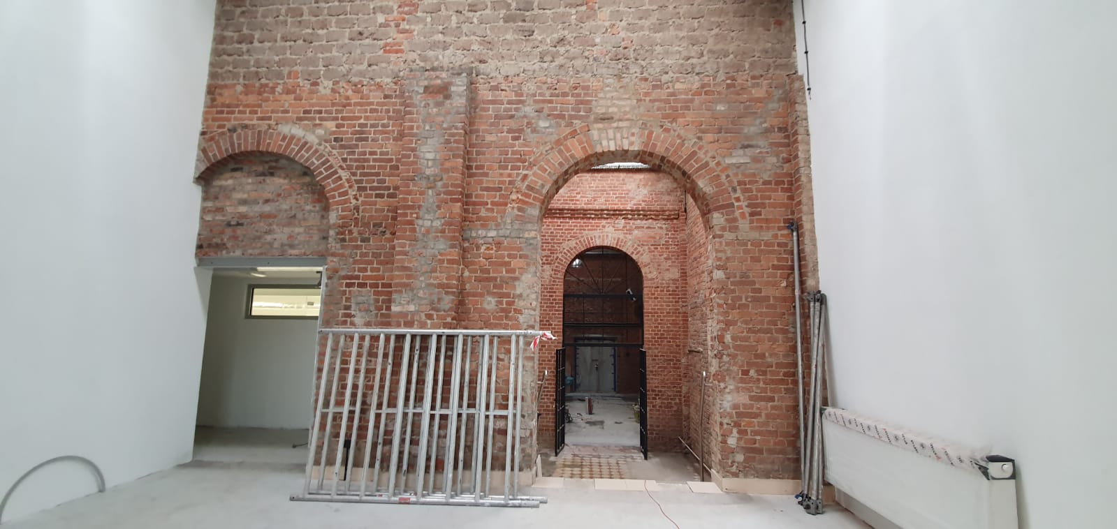 Ignacy 05 2020 7 Industrialne wnętrze, ściany z czerwonej cegły, stalowe konstrukcje. Po prawej i lewej stronie dwie otynkowane na biało ściany.